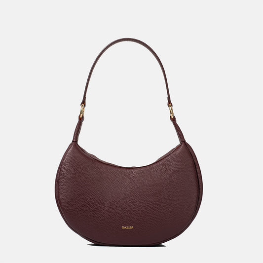 Bordowa skórzana torebka damska o półokrągłym kształcie z złotymi elementami i regulowanym paskiem.