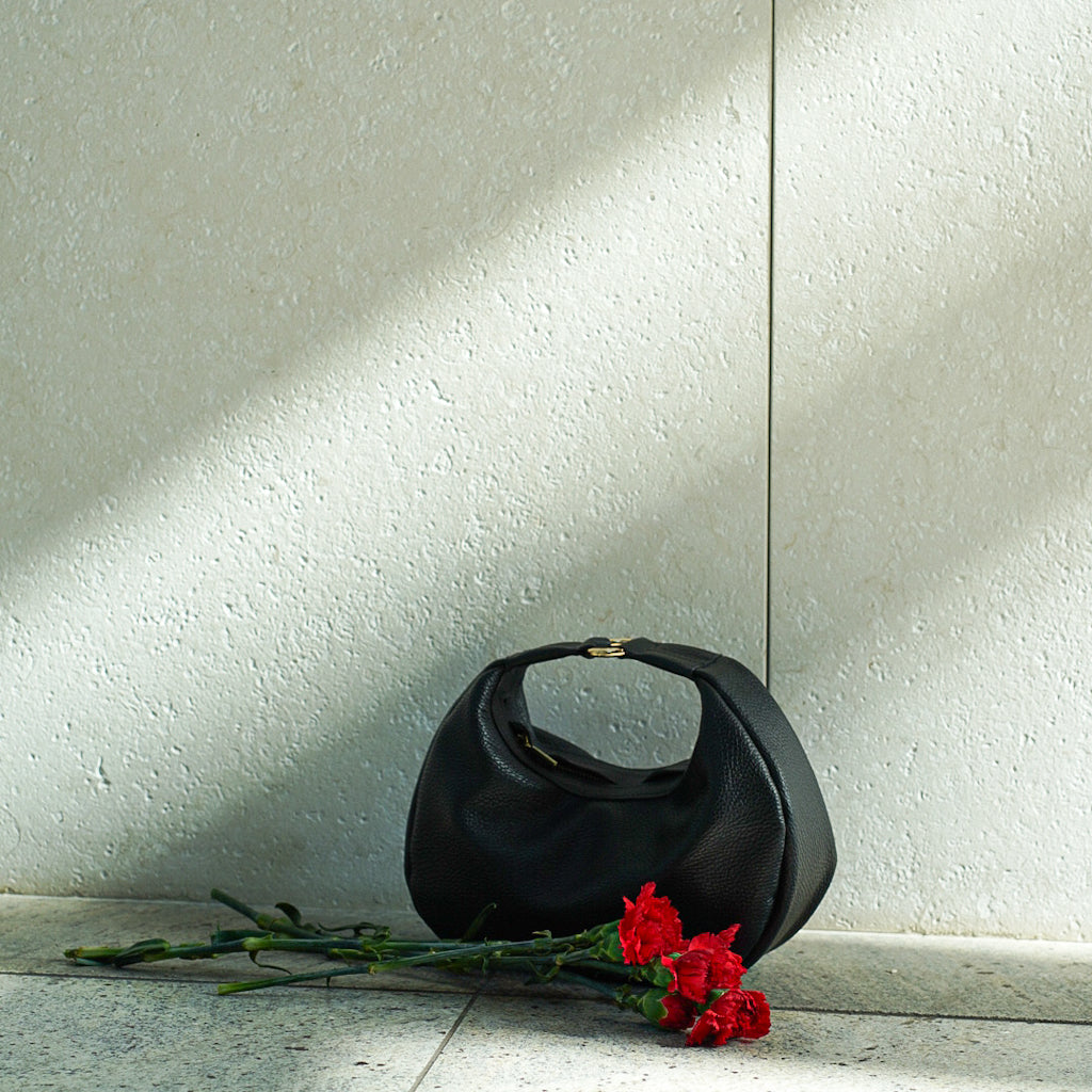 Czarna skórzana torebka Hedera obok czerwonych kwiatów na betonie
