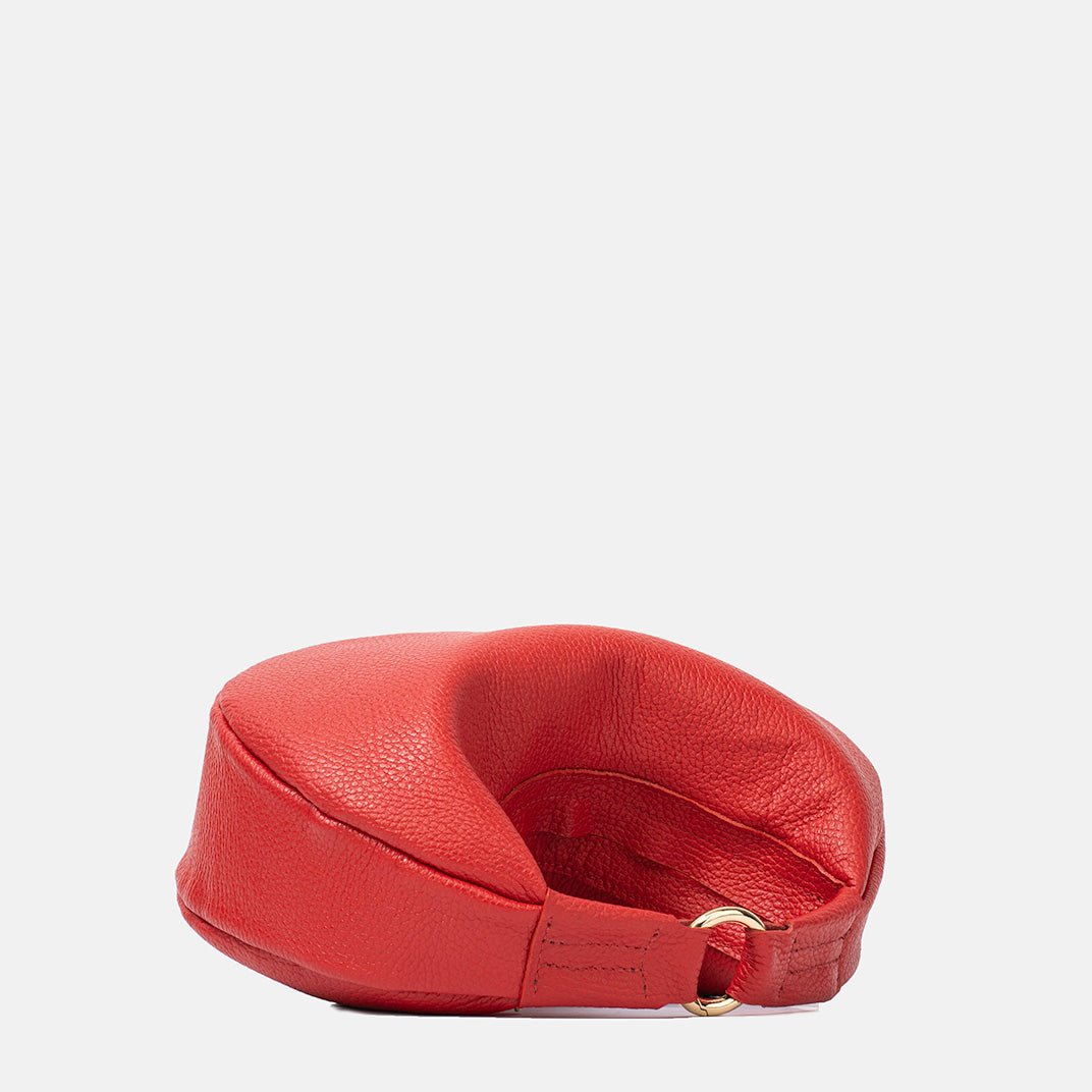 Górny widok czerwonej skórzanej torebki damskiej w kształcie półksiężyca, leżącej na boku z widocznym złotym zapięciem