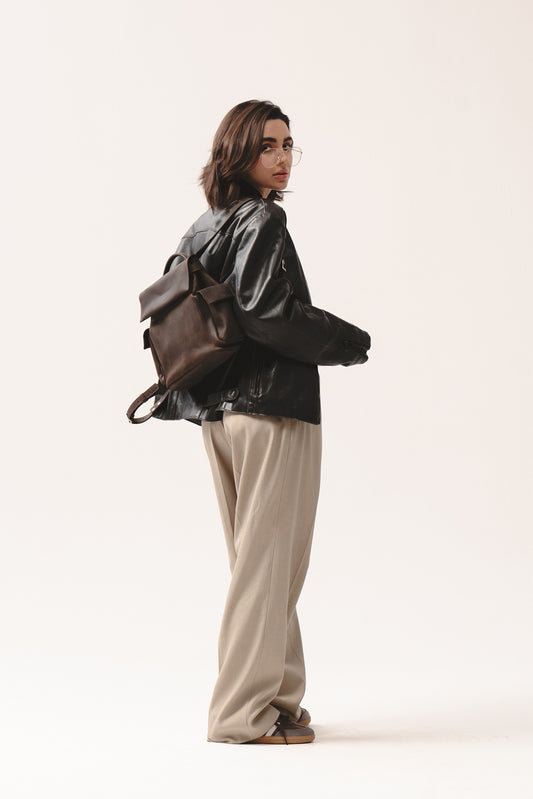 Ciemnobrązowy skórzany plecak EU marki Taksuba noszony na plecach przez kobietę w skórzanej kurtce i beżowych spodniach