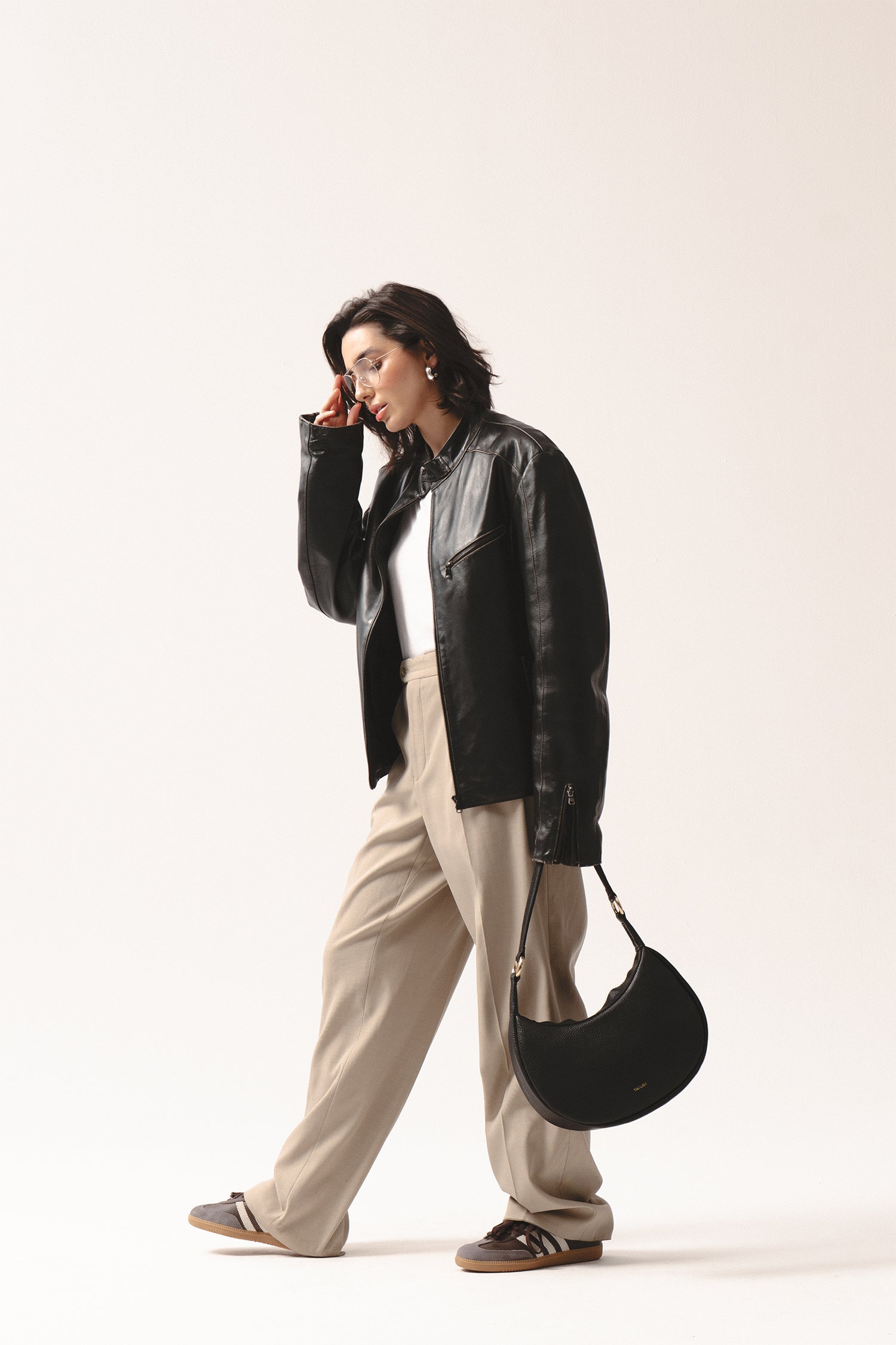 Skórzana torebka Hedera czarna crossbody na ramię, stylizacja z kurtką skórzaną i beżowymi spodniami