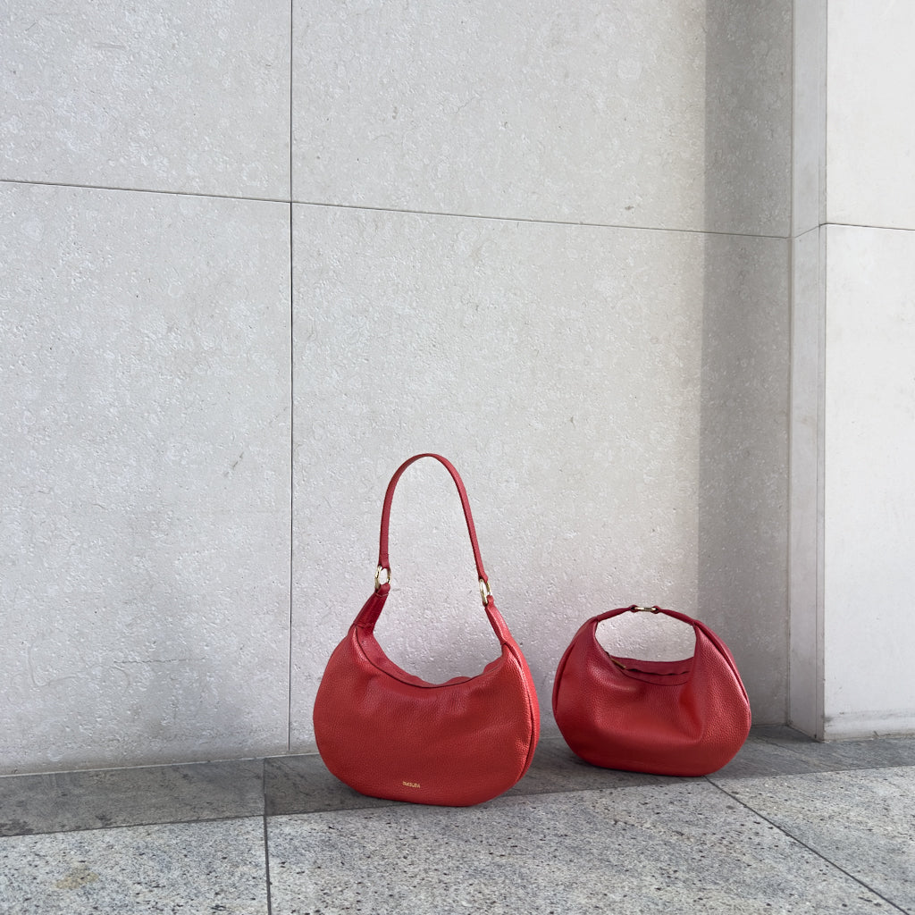 Czerwone torebki Hedera w dwóch rozmiarach na miejskim tle, wyrafinowany design