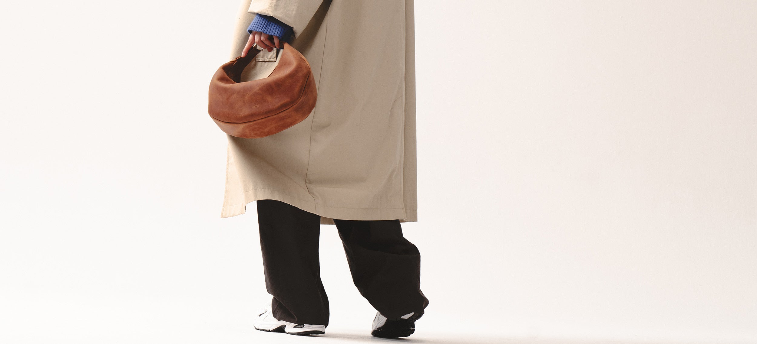 Osoba w trenczu trzymająca skórzaną torebkę Hedera w kolorze koniakowym brązie marki Taksuba