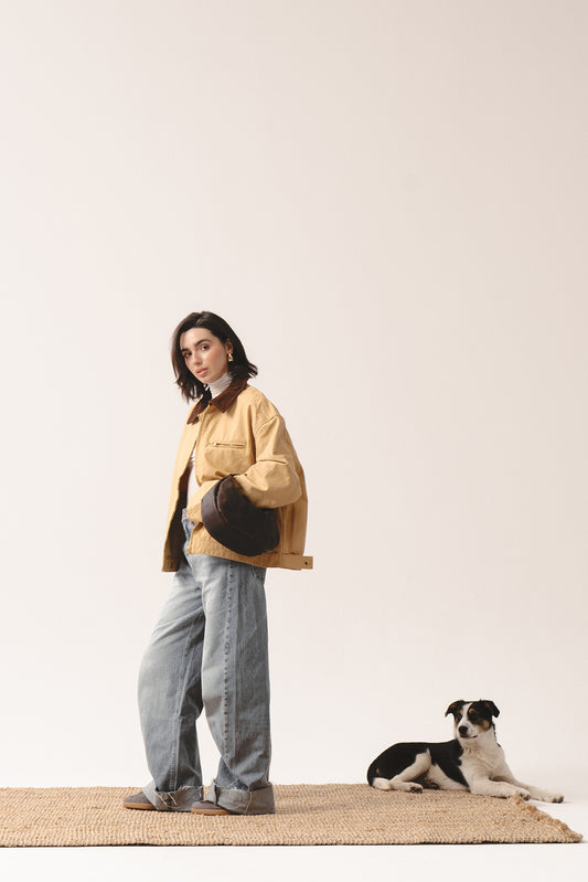 Ciemnobrązowa skórzana torebka Hedera marki Taksuba trzymana pod pachą przez kobietę w beżowej kurtce i dżinsach, z psem w tle