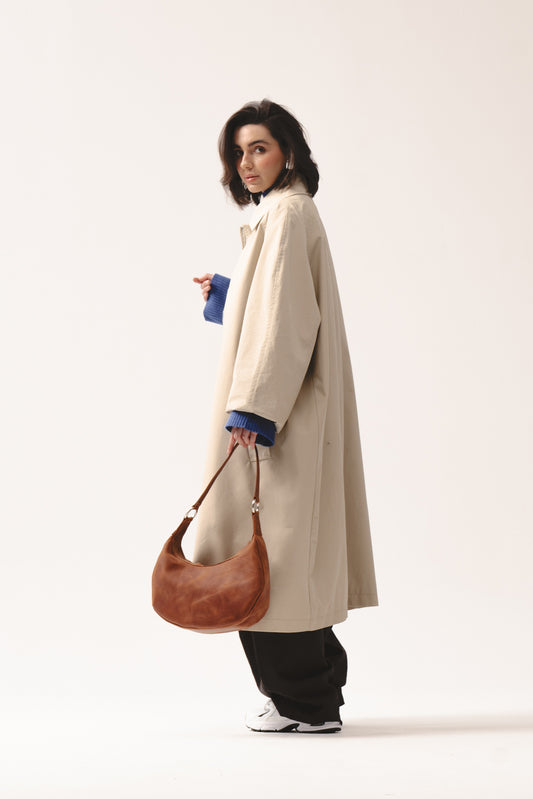 Skórzana torebka Hedera koniakowa marki Taksuba trzymana w dłoni przez kobietę w beżowym płaszczu