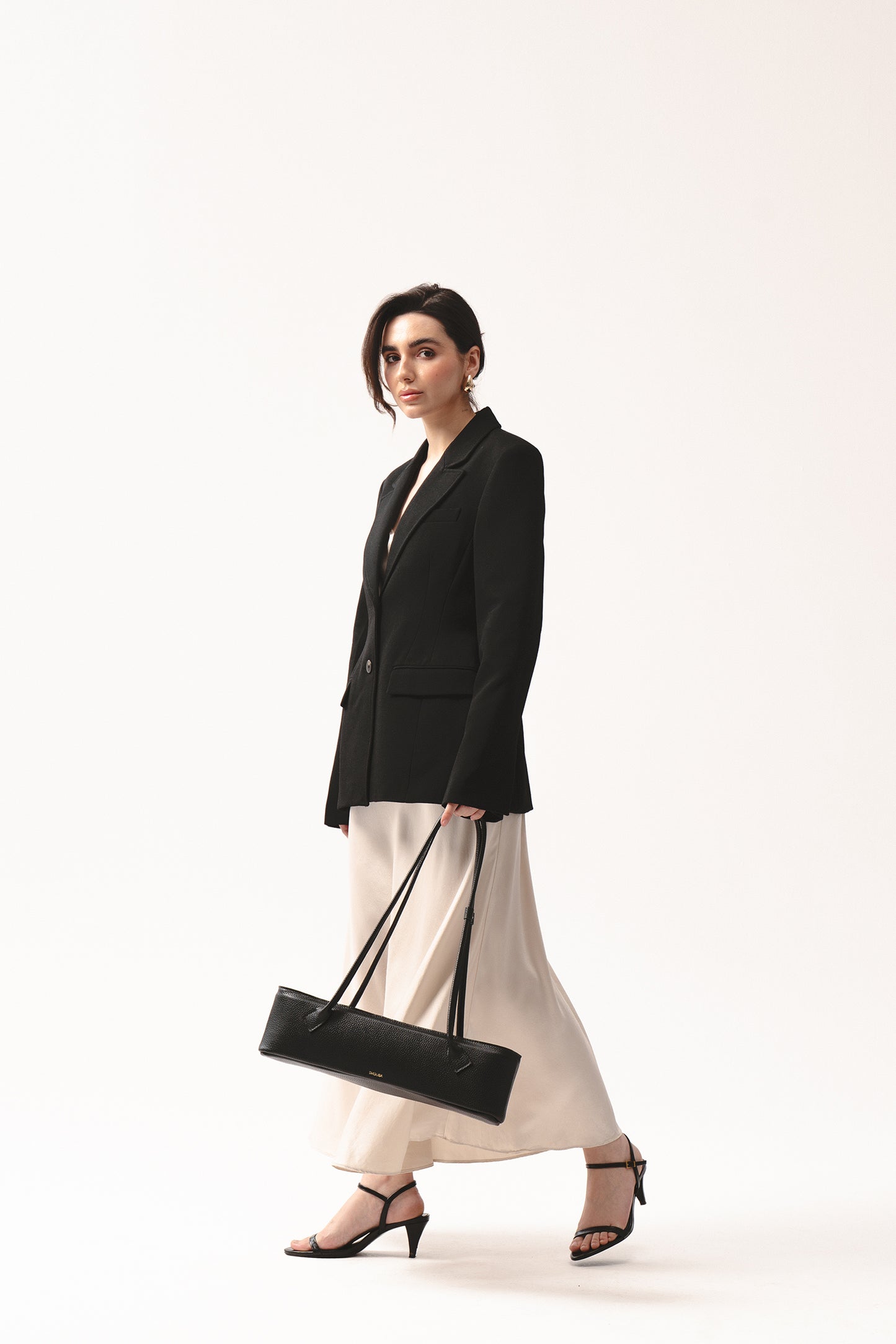 Podłużna czarna torebka Teckelete skórzana na długich rączkach w minimalistycznej stylizacji z marynarką