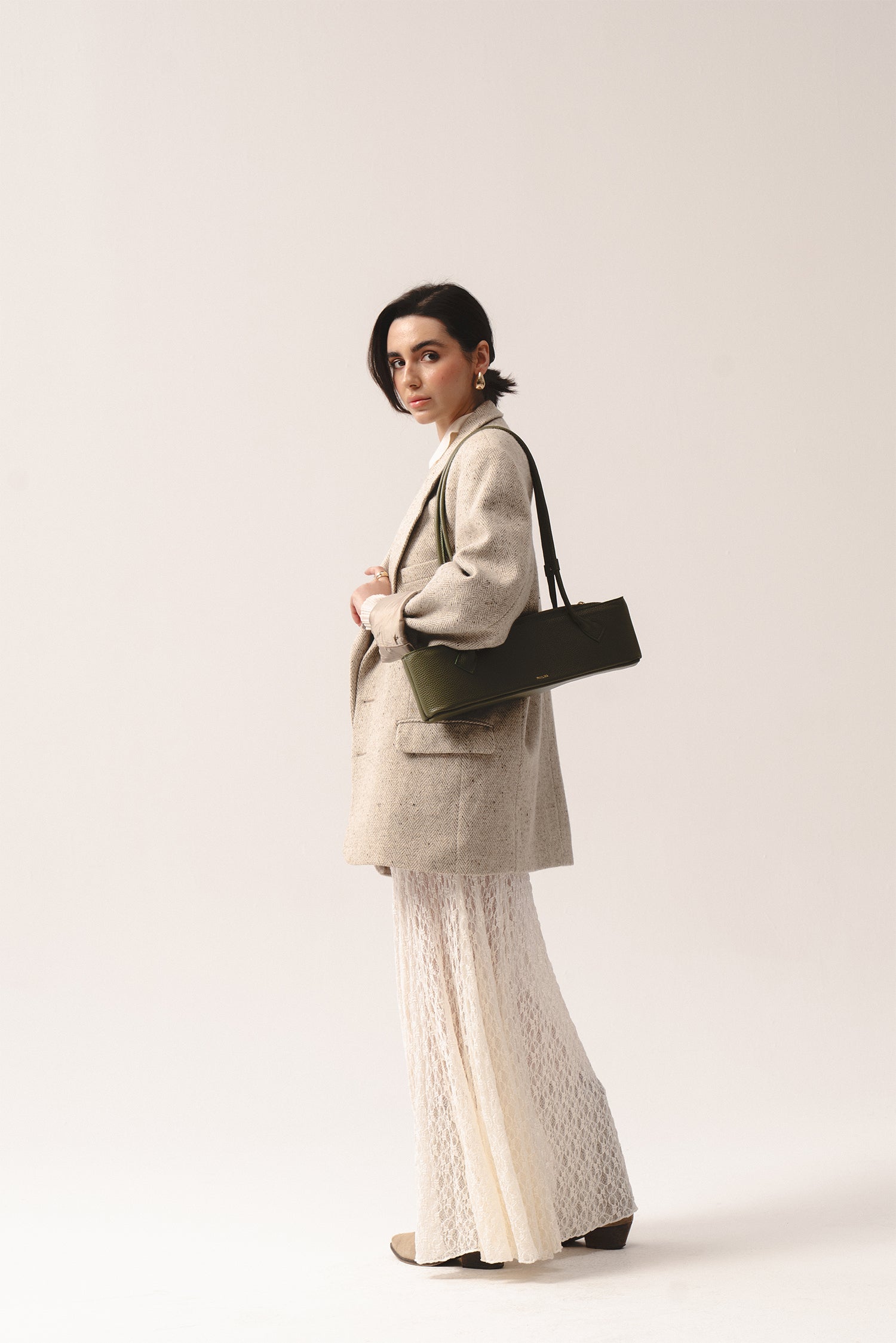 Torebka Teckelete w kolorze oliwkowym na ramieniu, stylizacja z beżowa marynarka i koronkową spódnicą