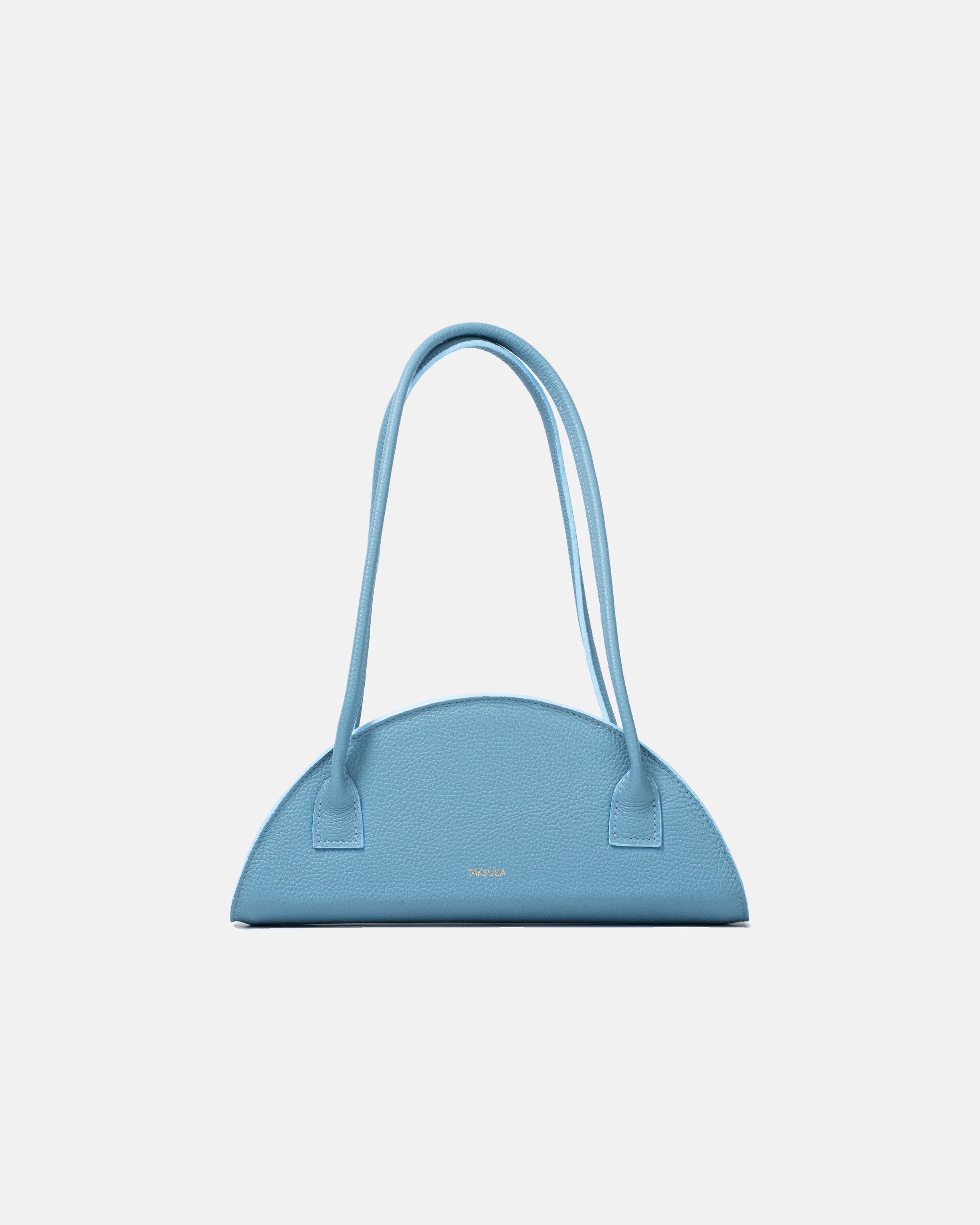 Półokrągła błękitna torba skórzana damska marki Taksuba z długimi uchwytami na ramię i złotym logo na przodzie.