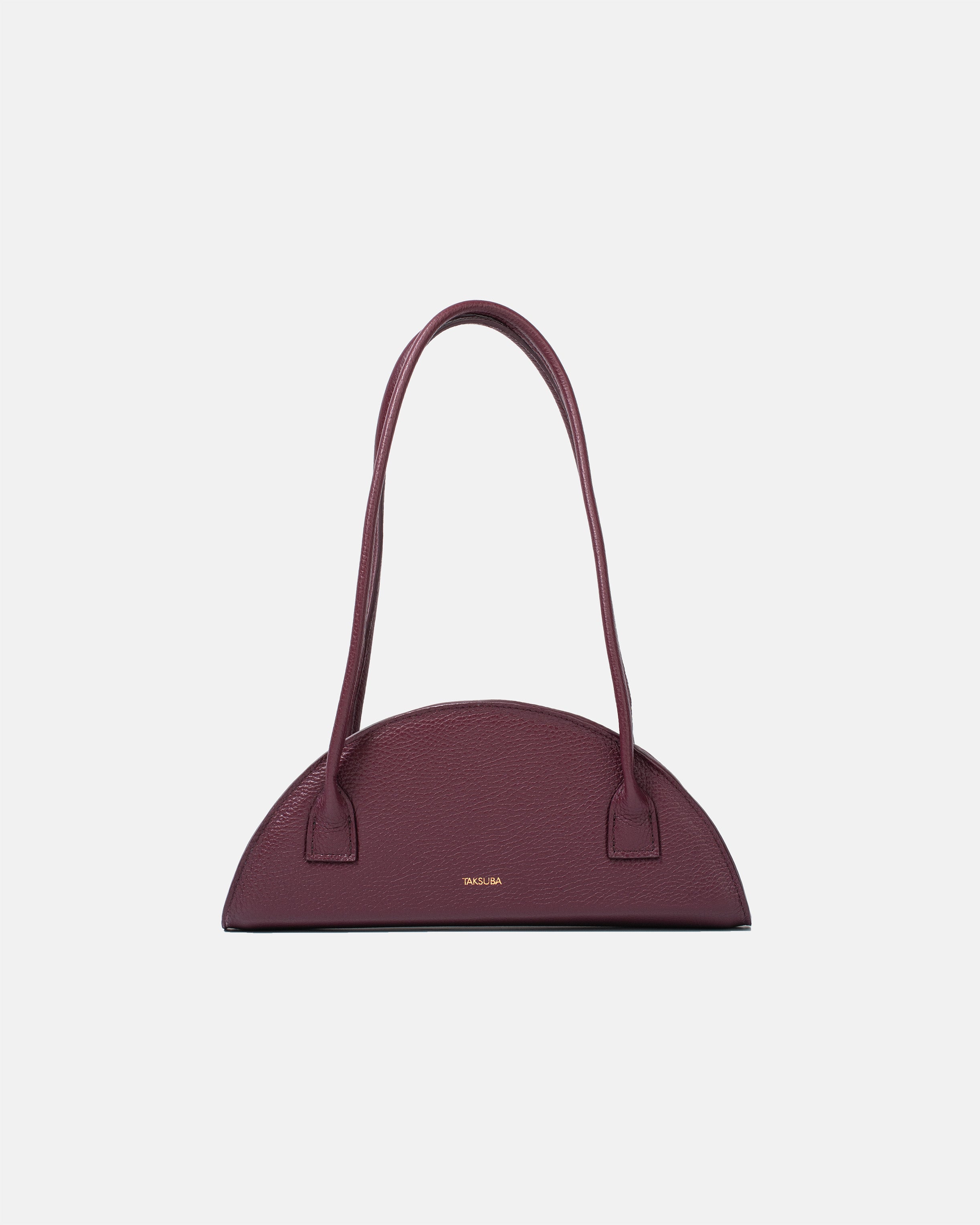Półokrągła bordowa torba skórzana damska marki Taksuba z długimi uchwytami i złotym logo na środku frontu.