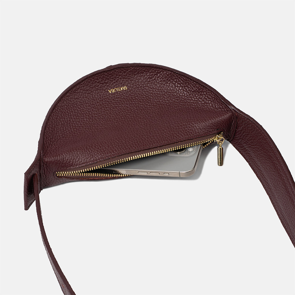 Bordowa skórzana torebka damska z zamkiem, złotymi suwakami, pokazująca wnętrze z telefonem.

