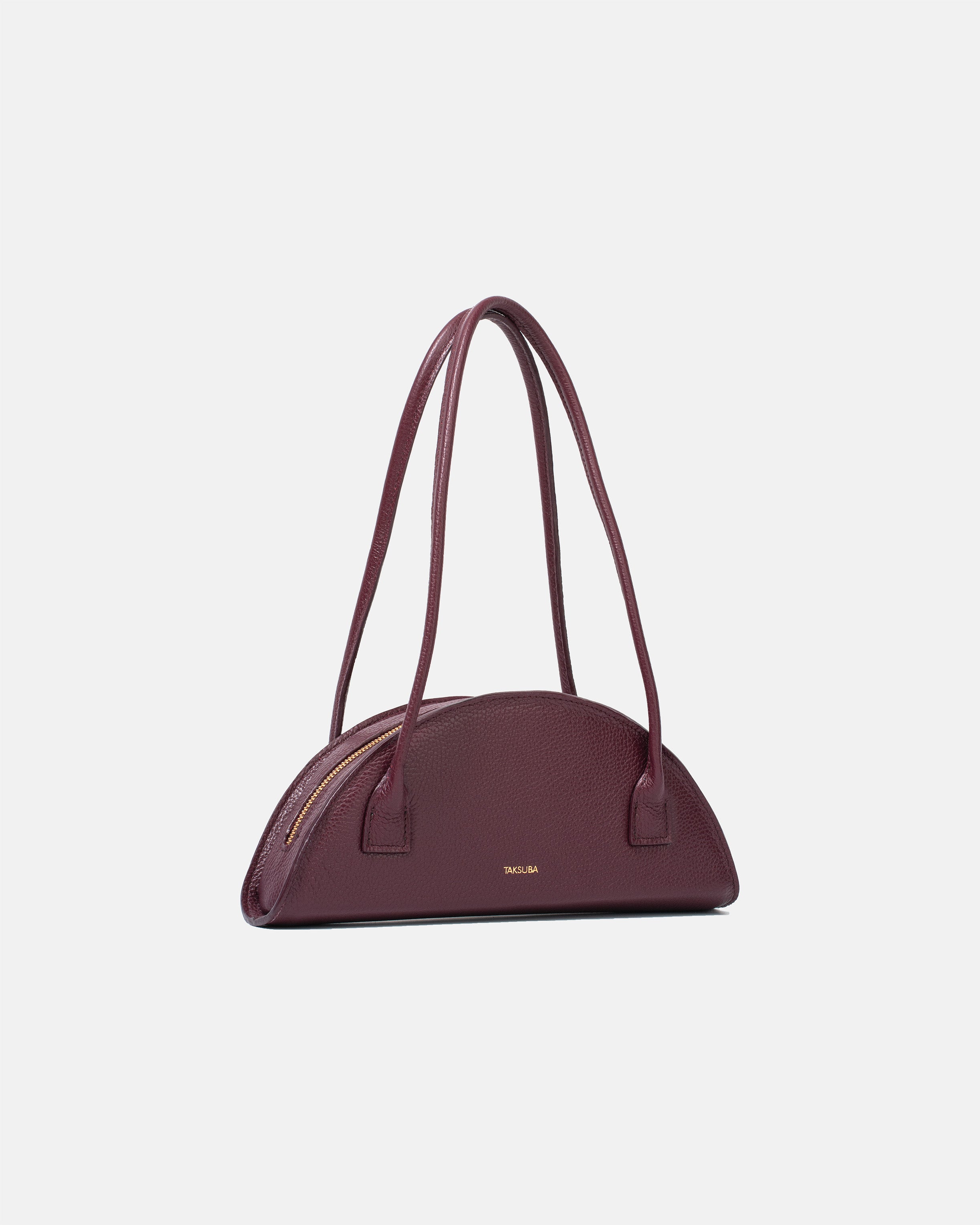 Bordowa torba skórzana damska marki Taksuba o półokrągłym kształcie, z widocznym złotym zamkiem i długimi rączkami.