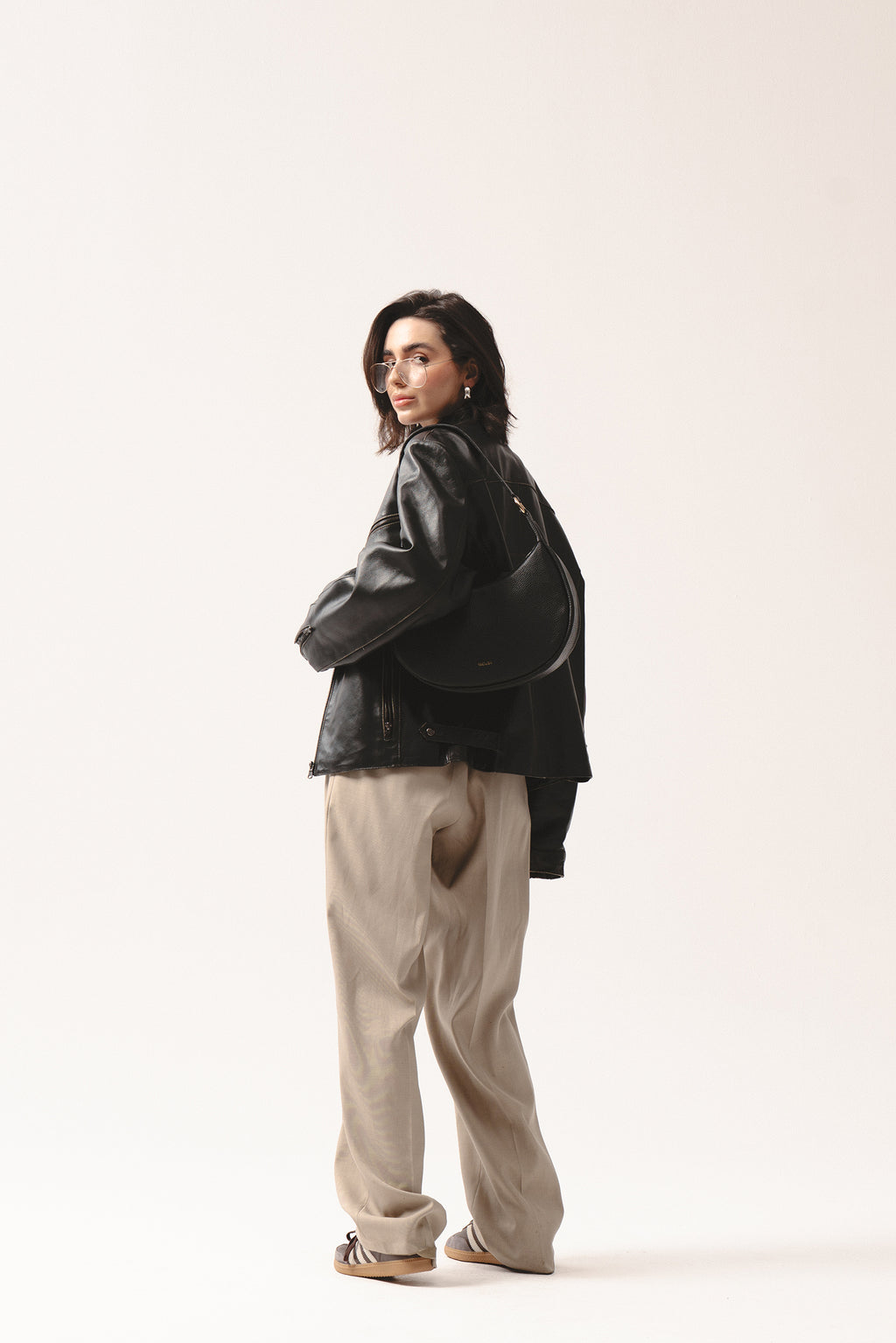 Skórzana torebka Hedera czarna na ramię, noszona z czarną kurtką skórzaną i beżowymi spodniami