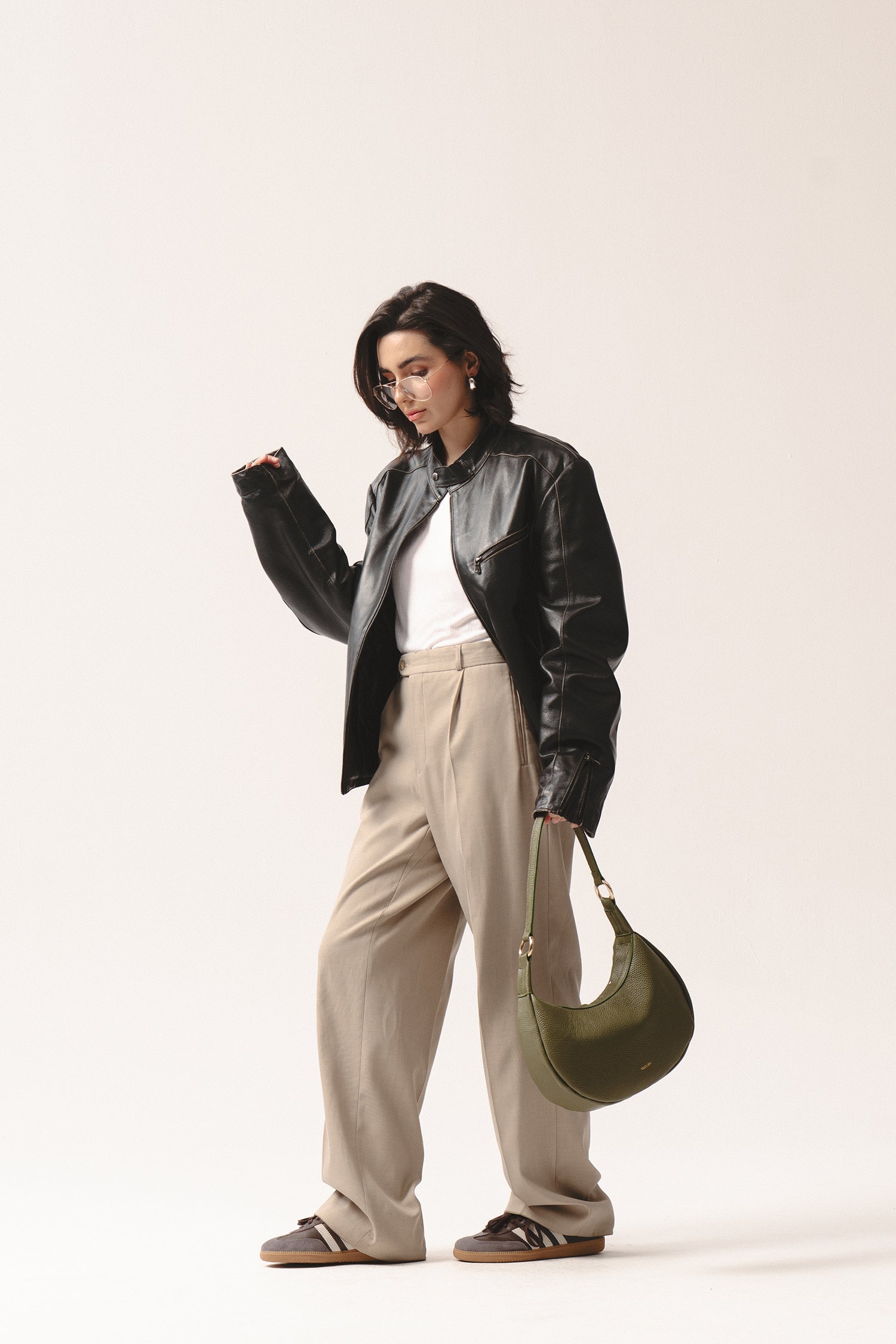 Skórzana torebka na ramię Hedera w oliwkowej zieleni – olive green crescent leather handbag styled with beige trousers and black jacket