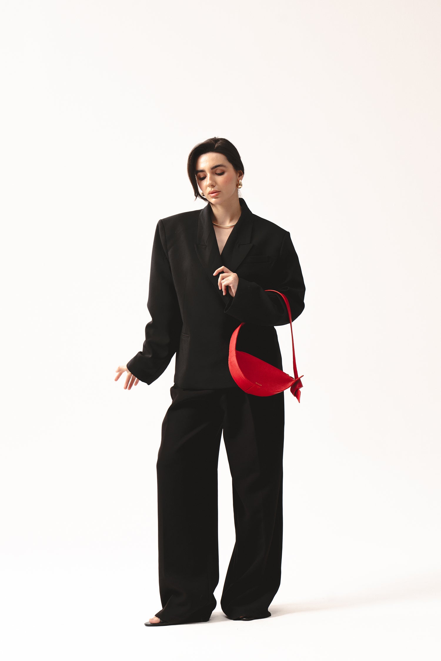 Skórzana torebka damska czerwona na ramię – mała elegancka półksiężycowa torba z naturalnej skóry, trzymana przez kobietę w czarnym garniturze.