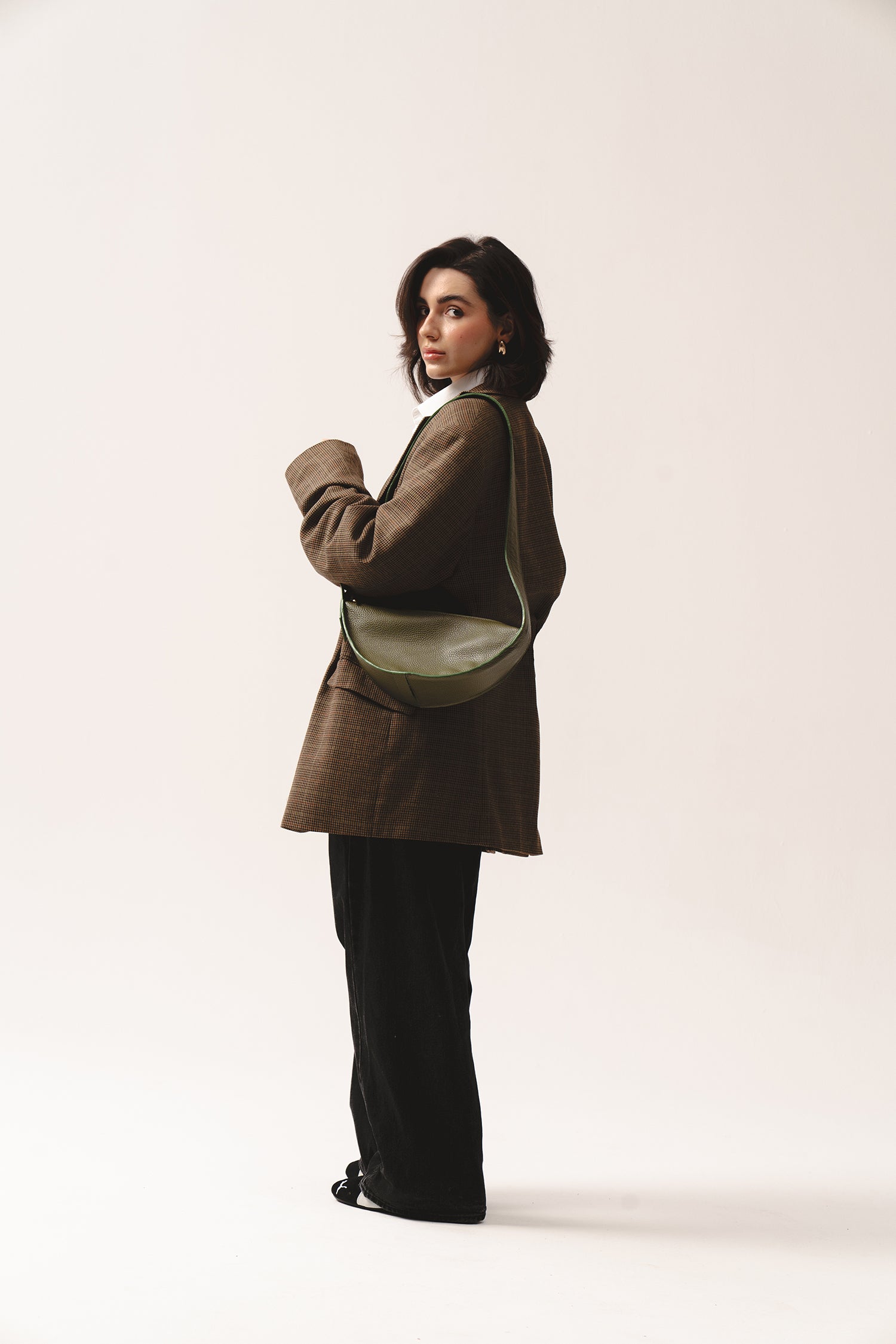 Torebka Eclipse M oliwkowozielona na ramieniu, zestawiona z marynarką w kratę i czarnymi spodniami