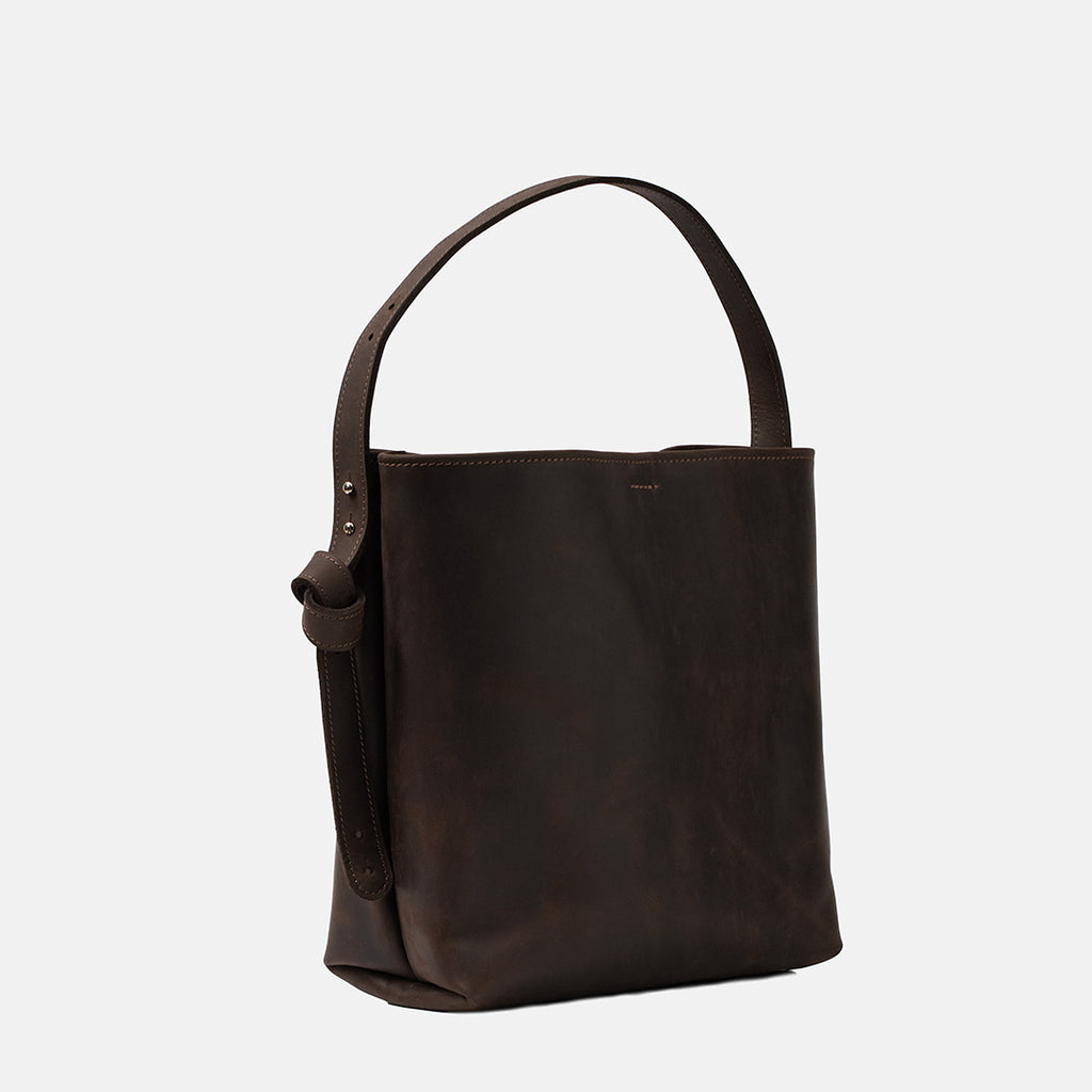 Ciemnobrązowa skórzana torebka shopper marki Taksuba z bocznym widokiem na regulowany pasek i surowe wykończenie