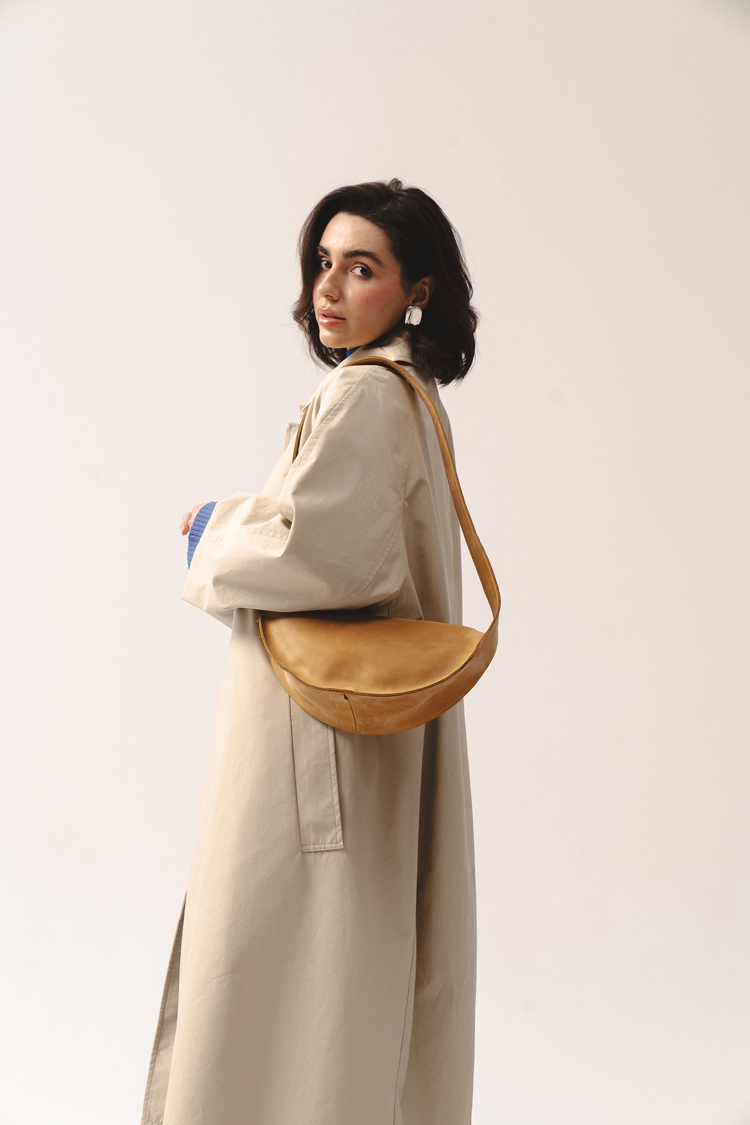 Skórzana torebka Eclipse M żółta noszona na ramieniu przez kobietę w beżowym płaszczu