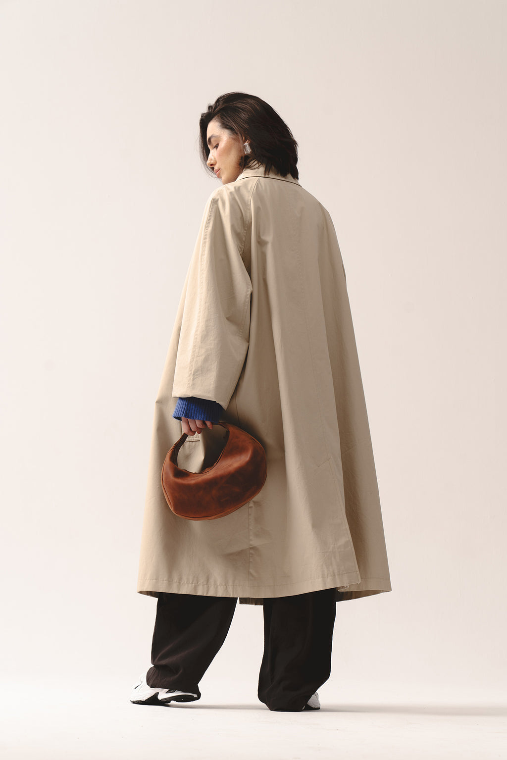 Skórzana torebka Hedera koniakowa trzymana w ręce jak clutch przez kobietę w beżowym płaszczu