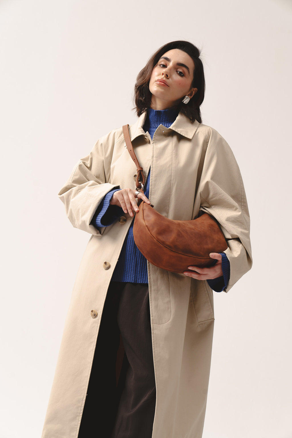 Skórzana torebka Hedera w kolorze koniakowym marki Taksuba, trzymana pod pachą przez kobietę w beżowym płaszczu