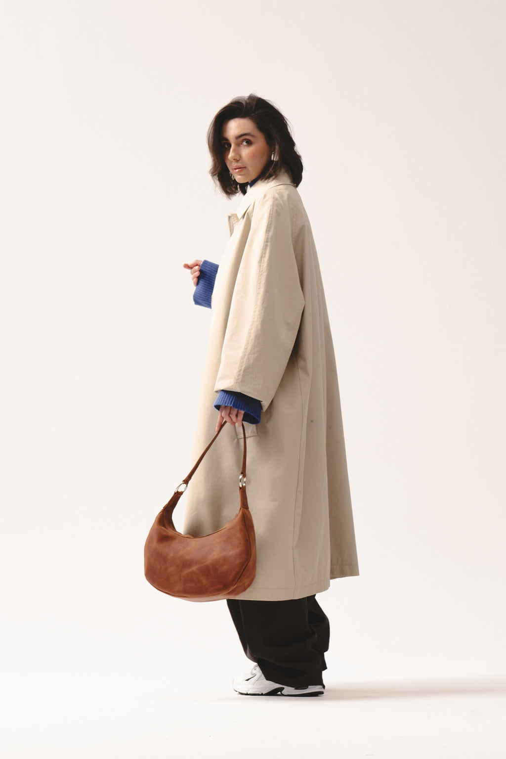 Skórzana torebka Hedera koniakowa marki Taksuba trzymana w dłoni przez kobietę w beżowym płaszczu