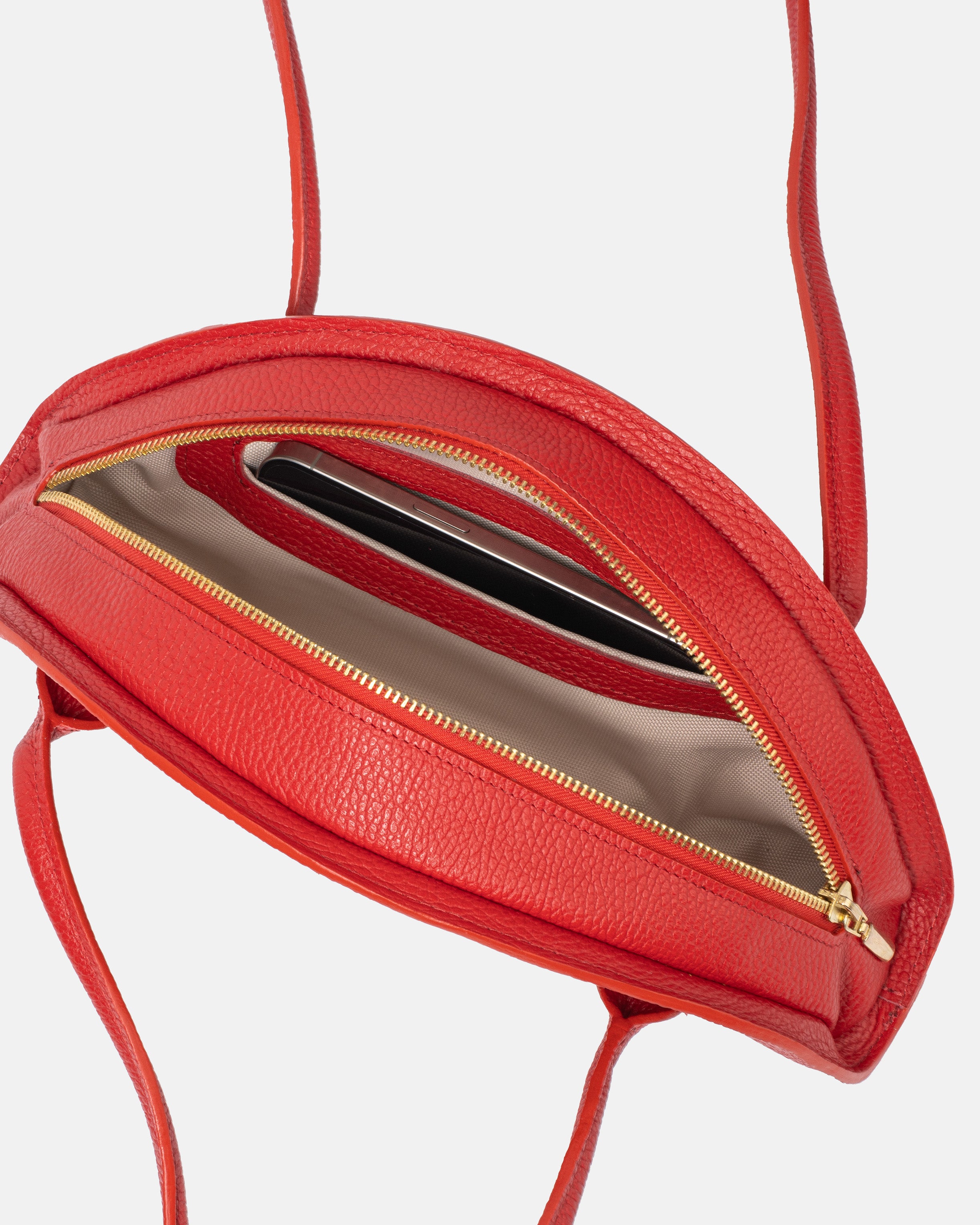 Wnętrze otwartej czerwonej skórzanej torby typu 'bowling', pokazujące przegrodę na telefon komórkowy i zamkiem błyskawicznym